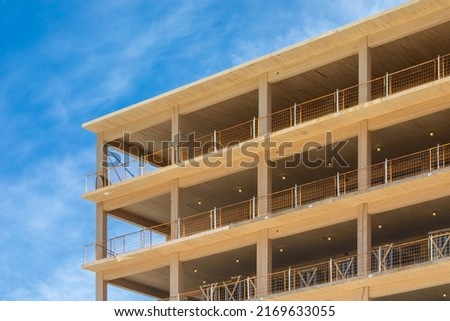 Looking up at the wooden balconies, the vertical supports and interior ceilings of a engineered timber multi story green, sustainable residential high rise apartment building construction project Royalty-Free Stock Photo #2169633055
