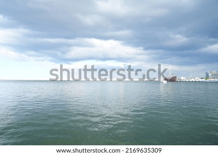 Seaside view of the polish harbor in Gdynia with calm water and cloudy sky with a small ship in the background