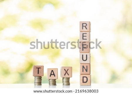 Tax refund word written on wood cubes, stacks of coins, nature green background.