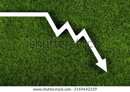 White chart arrow on green grass pointing down. Business loss symbol, ecology concept, green energy spending.