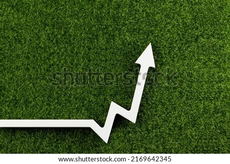 White chart arrow on green grass points up. Business development symbol, ecology concept, green energy.