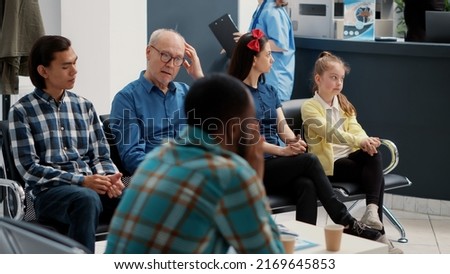 Different people waiting in row at hospital reception lobby to be called in office at checkup visit examination with specialist. Waiting room area for medical consultation at busy clinic. Royalty-Free Stock Photo #2169645853