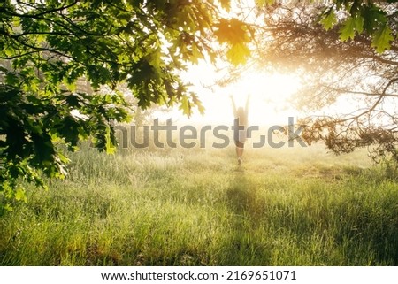 Woman with raised hands enjoy the beautiful forest at sunrise. Full body silhouette