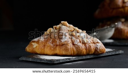 Baked croissant on a wooden board and sprinkled with powdered sugar, black table. Appetizing pastries for breakfast