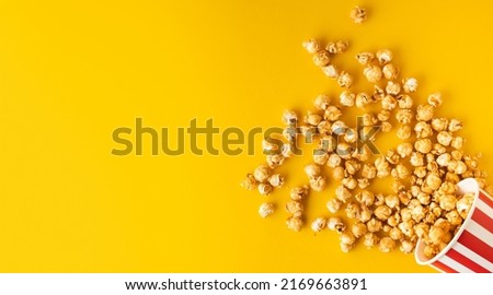 caramel popcorn scattered from a red and white bucket on a yellow background. Flat lay. cinema advertising. Copy space