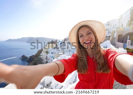 Traveler girl taking selfie photo in Santorini on sunset. Smiling woman having fun in Oia village in Greece.