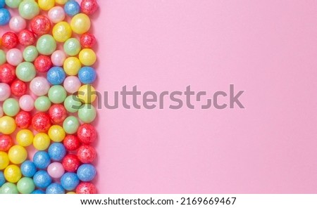 Multi-colored round glossy balls of sugar confectionery topping lie at the left on a pink background.