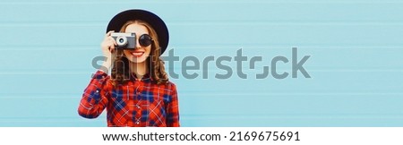 Portrait of happy smiling young woman photographer with film camera on blue background, blank copy space for advertising text