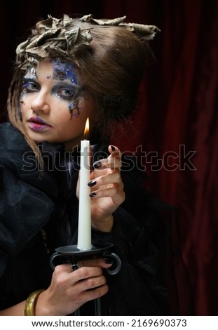 Beautiful woman in a witch costume with bright makeup and hairdo is holding a candle. Halloween. Party. Holiday. Carnival.