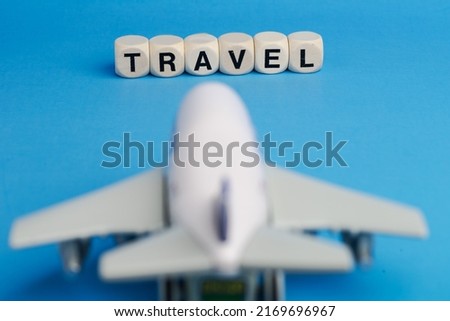 Traveling concept, wooden cubes with TRAVEL word and toy airplane on blue background.