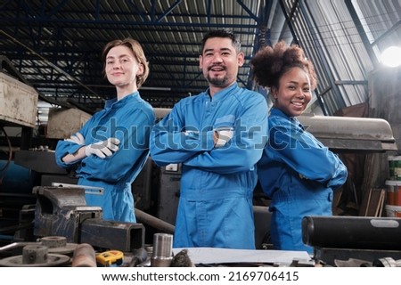 Multiracial industry workers in safety uniforms collaborate with unity, arms crossed, and express happy work together with smile and cheerful in mechanical factory, professional engineer occupation. Royalty-Free Stock Photo #2169706415
