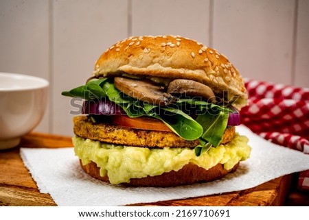 Vegan veggie protein burger, with tomato, arugula, red onion, mushrooms and avocado mayonnaise on a wooden board and a white background. Normal view. Copy text. Natural food concept, vegetarian.