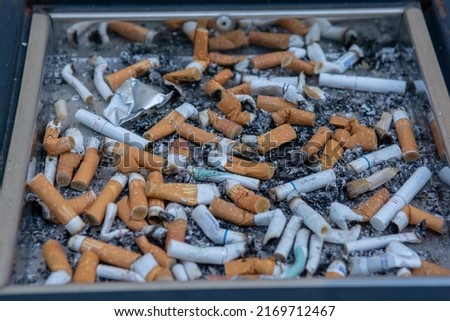 Many of cigarette butts in a big public ash tray.  Stacked cigarette butts. Royalty-Free Stock Photo #2169712467