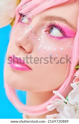 Beauty girl. Portrait of a beautiful girl with bright pink makeup and pink hair with floral wreath on her head. Japanese anime style. Spring and summer beauty. Blue background.