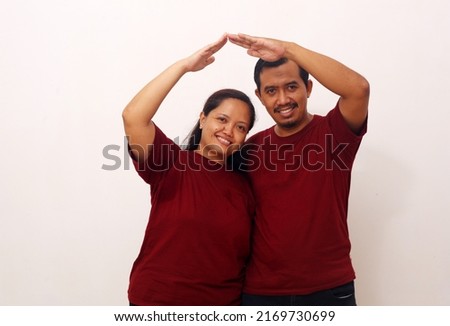 Happy Asian couple standing while making roof home gesture with hands arms. Isolated on white