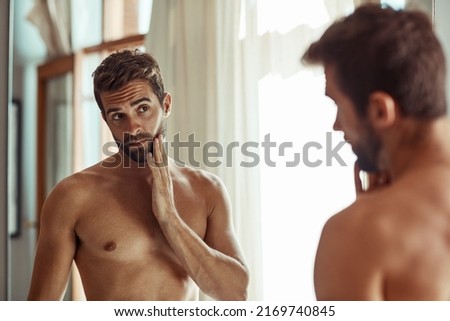 Keeping a close eye on any signs of aging. Shot of a shirtless man checking out his skin in the bathroom mirror. Royalty-Free Stock Photo #2169740845
