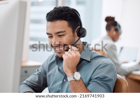 Offering clear advice and instruction to a caller. Shot of a young call centre agent working in an office with his colleague in the background. Royalty-Free Stock Photo #2169741903
