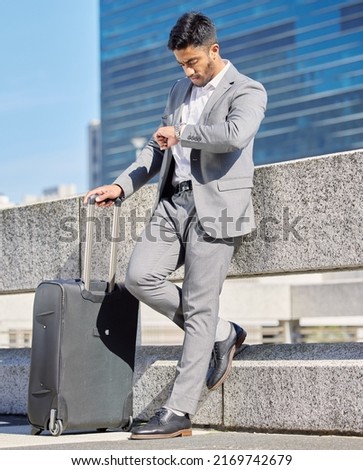 I hope Im not going to be late. Shot of a young businessman checking the time while standing with a suitcase in the city.