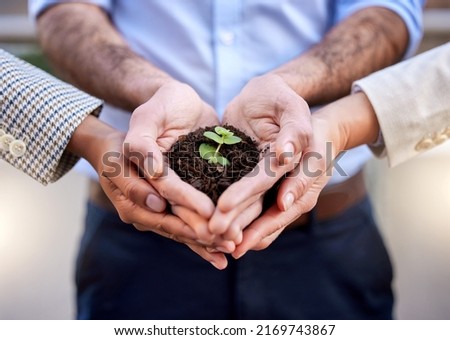 Were all here to help it grow. Shot of a group of unrecognizable businesspeople holding a plant in soil at work.