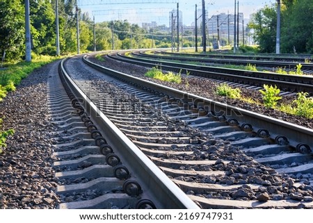 Closeup of the railroad tracks of a multi-lane railway stretching into the distance against the backdrop of a summer morning city on the horizon. Royalty-Free Stock Photo #2169747931
