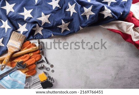 Happy Labor day concept during coronavirus disease (Covid-19). American flag with different construction tools and medical mask on dark stone background.
