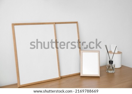 Blank frames with reed diffuser and tissue box on table near light wall