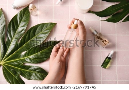 Female hands with bottles of natural serum, cosmetics and plant leaves on color tile