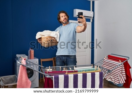 Handsome middle age man holding laundry basket doing selfie picture skeptic and nervous, frowning upset because of problem. negative person. 