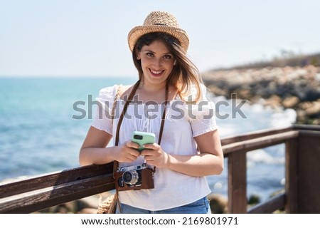 Young hispanic woman tourist smiling confident using smartphone at seaside