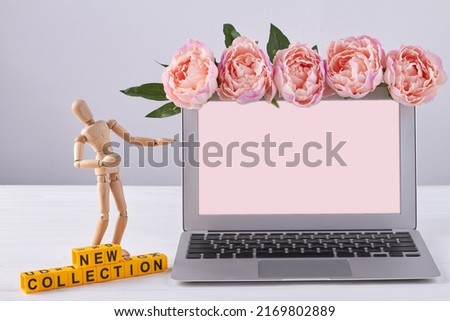 Laptop screen for copy space and wooden mannequin. New collection concept. Pink peony flowers.