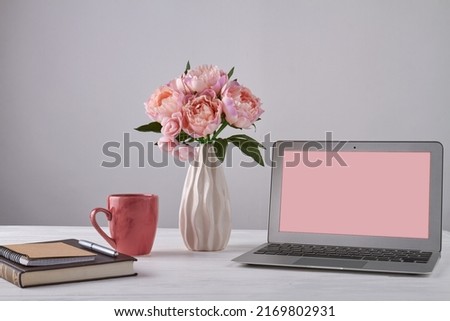 Vase of flowers with notepads and laptop with copy space. Notebook with pen and red cup.