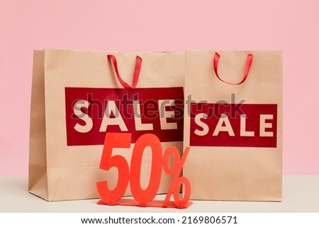 Close-up of shopping bags with Sale lettering and fifty percent tablet for store display window
