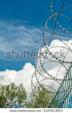 A fence with barbed wire on a blue sky background. Restricted passage area