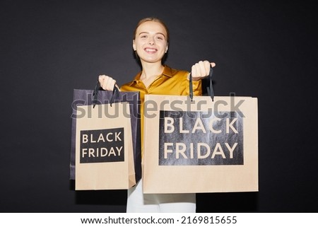 Smiling attractive young woman holding paper bags while being satisfied with best buy at Black friday