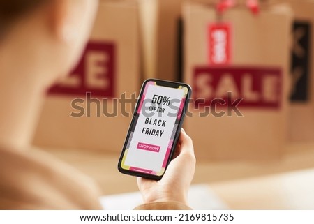 Over shoulder view of unrecognizable woman viewing bright online shopping poster on smartphone