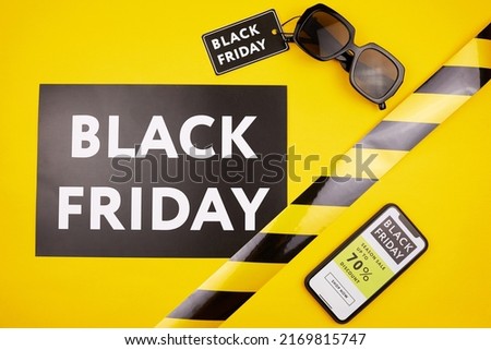 High angle view of Black Friday banner and sunglasses with tag on yellow background, online website on smartphone screen