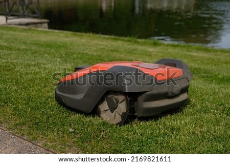 Robotic Lawn Mower on green grass background.Automatic robot lawnmower in modern garden.Green grass trimming with lawn mower. Close-up view of the lawn mower dirty blade after mowing the lawn. 