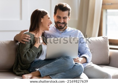 Overjoyed millennial couple relax at home have fun laugh browsing internet on modern computer gadget. Smiling young Caucasian man and woman enjoy weekend use laptop together. Technology concept. Royalty-Free Stock Photo #2169827639