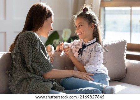 Happy young Caucasian mother and teen daughter sit relax on sofa talking sharing secrets. Smiling mom or nanny and teenage girl child rest on couch speak enjoy family weekend bonding at home. Royalty-Free Stock Photo #2169827645