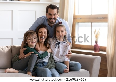Portrait of happy young Caucasian family with two teen children sit relax on sofa in living room enjoy weekend together. Smiling parents rest on couch at home with small kids have fun indoors.