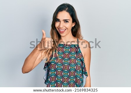 Young hispanic girl wearing casual clothes smiling happy and positive, thumb up doing excellent and approval sign 