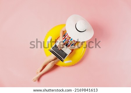 Top view full body young woman in striped swimsuit lies on inflatable rubber ring pool hold use work on laptop pc computer isolated on plain pink background. Summer vacation sea rest sun tan concept
