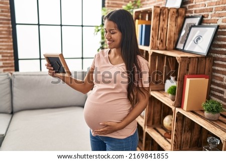 Young latin woman pregnant looking photo at home