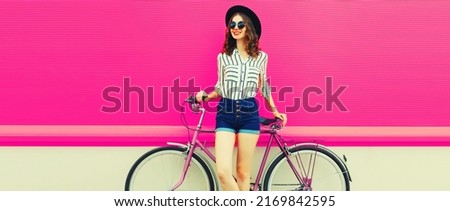 Summer colorful portrait of happy smiling young woman with bicycle in the city on pink background