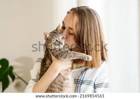 Indoor shot of amazing lady holding pet. Portrait of young woman holding cute striped cat with green eyes. Female hugging her cute kitty. Adorable domestic pet concept. Indoor shot of amazing lady Royalty-Free Stock Photo #2169854561