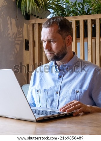 Serious handsome arabian man with beard is using laptop, reading email, typing on keyboard in cafe. Handsome male freelancer working on laptop at workplace. Businessman typing information