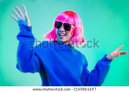 Young asian woman in blue sweatshirt pink short hair punk style wearing sunglasses posing dancing on the green screen background.