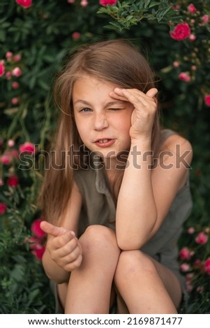 very beautiful little girl near the roses pricked with a thorn