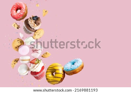 Colorful decorated Broken chocolate chip cookies, cupcakes and macaroons falling in motion on pink background with sprinkling and pieces with crumbs. Sweet and various pastries flying. Royalty-Free Stock Photo #2169881193