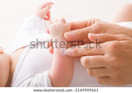 Young adult mother finger applying white medical ointment on newborn arm. Red rash on skin. Allergy from milk formula or mother milk. Care about baby body. Closeup. Side view. Royalty-Free Stock Photo #2169909661